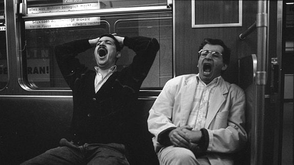 Zwei Männer gähnen in der U-Bahn.