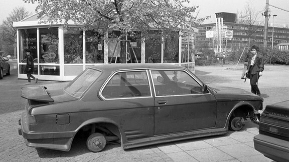 Auf einem Gehweg steht ein BMW, dessen Räder abmontiert sind.