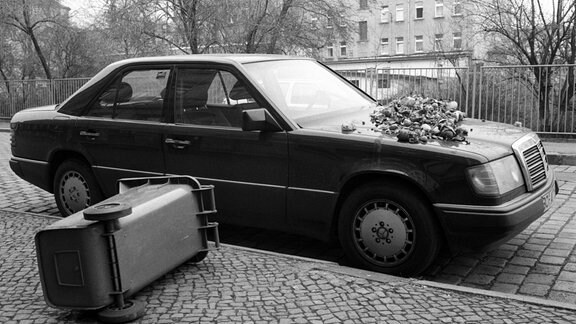 Neben einem Mercedes, auf dessen Kühlerhaube ein Haufen Abfall liegt, liegt eine umgekippte Mülltonne