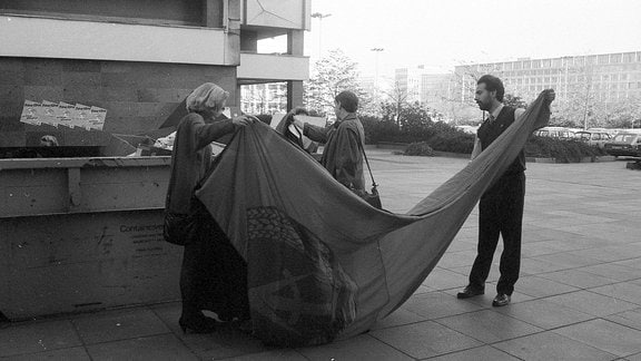 Neben einem Müll-Container der Leipziger Uni entfalten Neugierige eine große Flagge, die sie aus dem Container gefischt haben