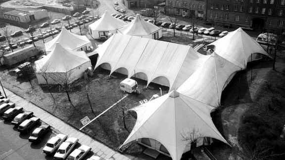 Blick auf eine Reihe von Zelten auf einer Freifläche wischen zwei Häuserreihen.