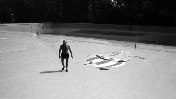 Ein Mann in kurzen Hosen läuft durch ein leeres Schwimmbadbecken, auf dessen Boden Obelix gemalt ist.