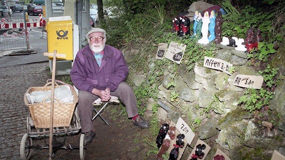 Ein bärtiger alter Mann verkauft Keramikfiguren zum  Stückpreis von fünf bis sieben Mark