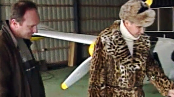 Eine Frau im Pelz und ein Mann vor einem Flugzeug