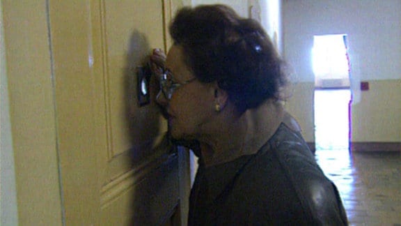 Eine Frau sieht durch einen Türspion.