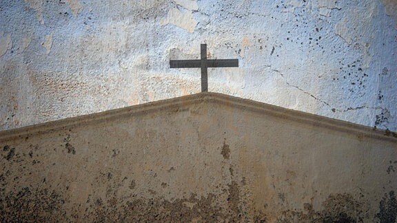 Auf eine rissige Häuserwand wurde ein Kirchedach mit einem Kreuz gezeichnet.