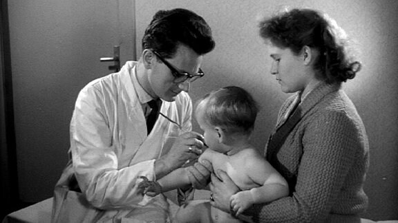 Arzt untersucht Schulter eines kleinen nackten Jungen, den die Mutter auf dem Schoß hält