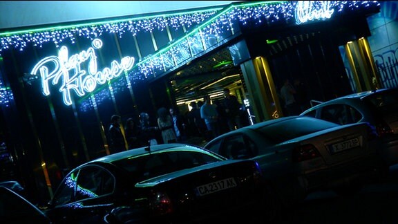Autos bei Nacht vor Diskothekenbeleuchtung.