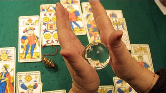 Hände halten eine Glaskugel über Tarotkarten