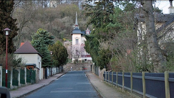 Blick auf eine Straße, an deren Ende ein Haus mit einem Turm steht.