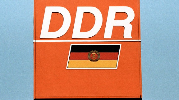 DDR-Schriftzug und Fahne auf orangefarbenem Grund