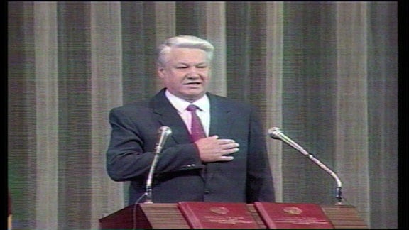 Boris Jelzin steht an einem Rednerpult. Während er spricht, hat er seine rechten Hand auf seine Brust gelegt.