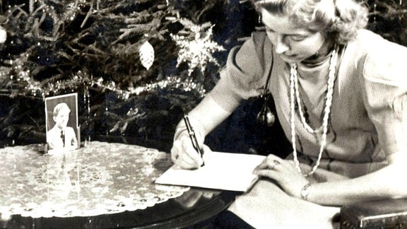 Eine Frau schreibt einen Brief vor einem Weihnachtsbaum