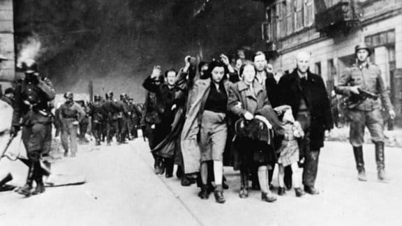 Menschen werden mit erhobenen Händen 1942 von bewaffneten Soldaten duch das Warschauer Ghetto getrieben