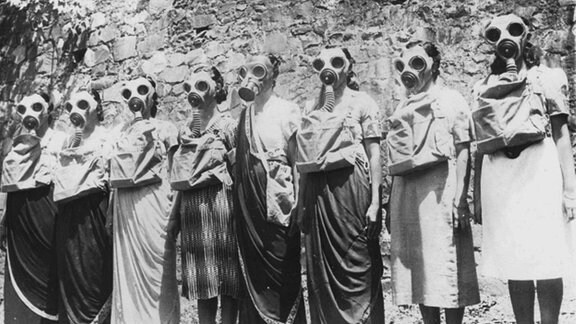 Frauen mit Gasmasken stehen in einer Reihe.