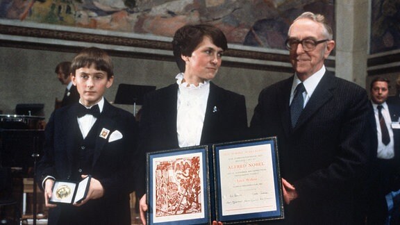 Die Ehefrau des polnischen Arbeiterrechtlers, Danuta Walesa, und ihr Sohn Bogdan nehmen den Friedensnobelpreis am 10. Dezember 1983 in Oslo stellvertretend entgegen, rechts der Vorsitzende des Nobelpreiskomitees in Stockholm, Egil Aarvik. 