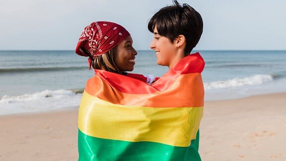 Lesbisches Paar umwickelt mit Regenbogenflagge an einem Strand