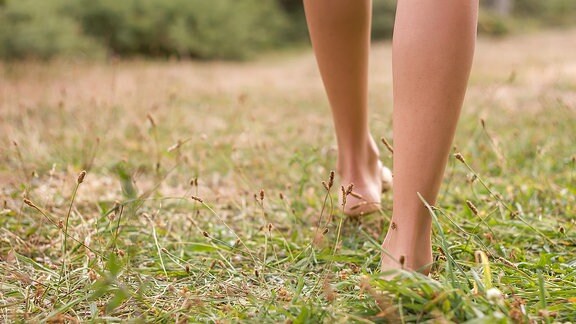 Die Füße einer barfuß über einen Rasen laufenden Frau.