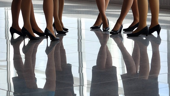 Frauenbeine auf einem spiegelnden Fußboden.