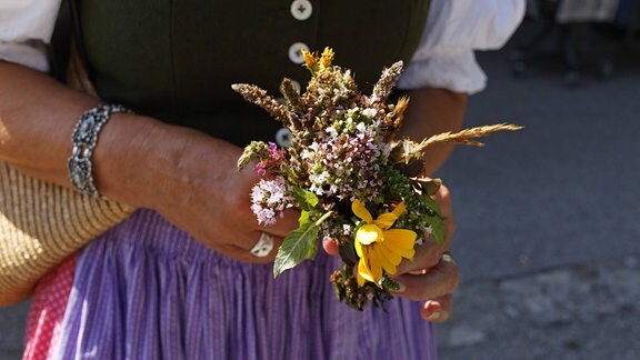 Eine Frau hält einen sogenannten Kräuterbuschen, einen Straß aus verschiedenen Sommerkräutern, in der Hand