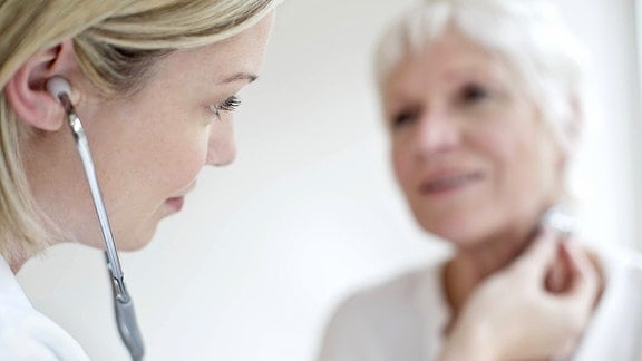 Ein Ärztin führt bei einer älteren Frau eine Schilddrüsenuntersuchung durch