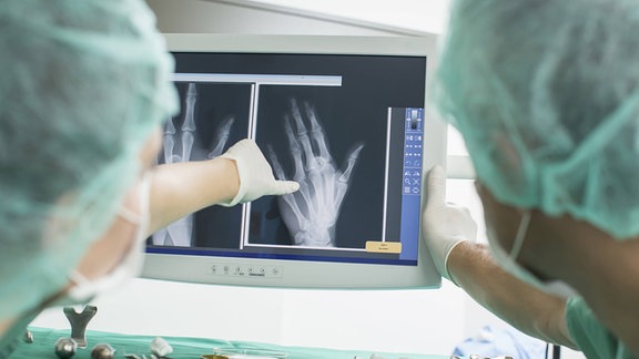 Zwei Handchirurgen in OP-Kleidung betrachten Röntgen-Aufnahmen. 