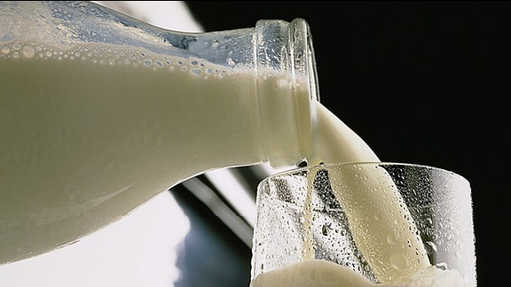 Milch fließt aus Milchflasche in ein Glas