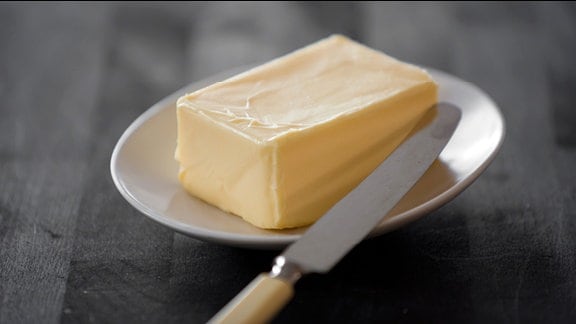 Ein Stück Butter liegt neben einem Messer auf einem Teller
