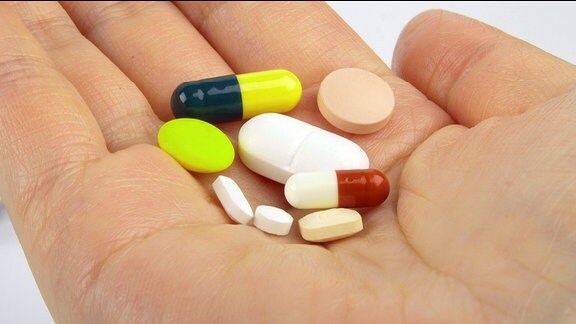 Eine aufgehaltene Hand mit verschiedene Tabletten.