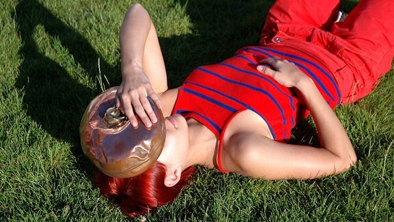 Eine junge Frau liegt auf einer Wiese und kühlt sich den Kopf