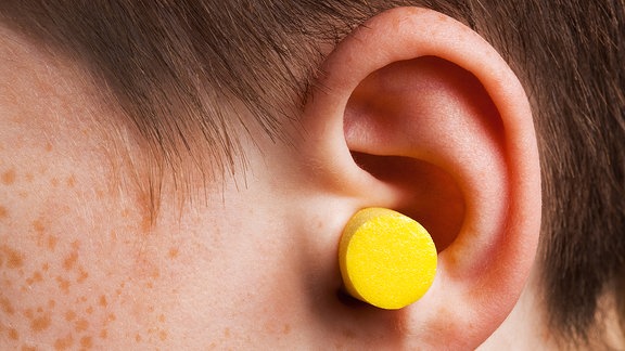 Ein gelber Ohrstöpsel steckt in einem Ohr.