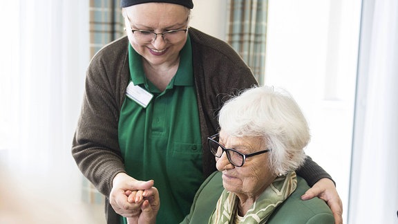 Lächelnde Pflegerin bei einer älteren Dame im Rollstuhl