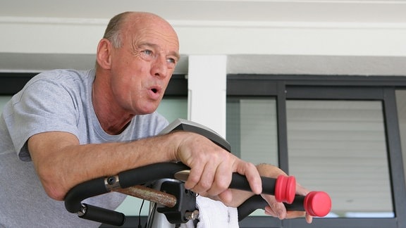 Ein Rentner sitzt in einem Fitnessstudio an einem Ergometer