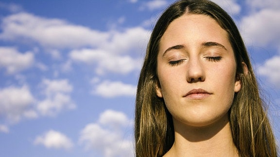 Eine junge Frau lässt sich mit geschlossenen Augen die Sonne aufs Gesicht scheinen.