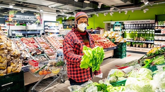 Ein Mann ist im Supermarkt mit Mundschutz einkaufen.