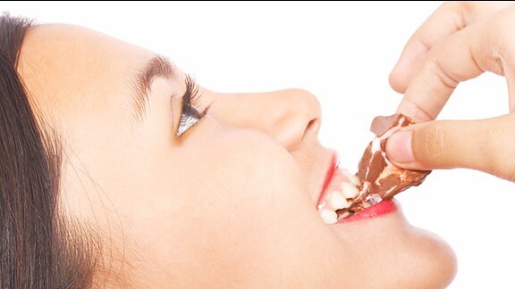 Eine Frau beißt von einem Stück Schokolade ab