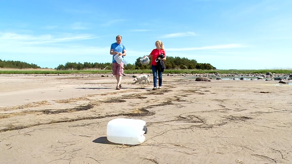 Mann und Frau am Strand. Sie sammeln Plastikmüll ein.