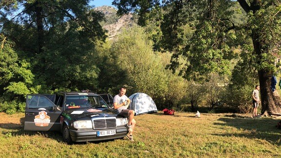 Auto mit offenen Türen neben Zelt auf Campingplatz unter Bäumen