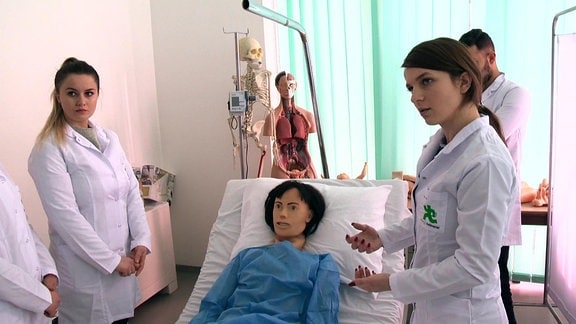 Junge Frauen im Kittel stehen um einen Patienten herum.