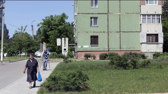 Ein ältere Frau mit blauem Einkaufsbeutel geht durch eine heruntergekommene Plattenbausiedlung aus der Sowjetzeit in Tiraspol