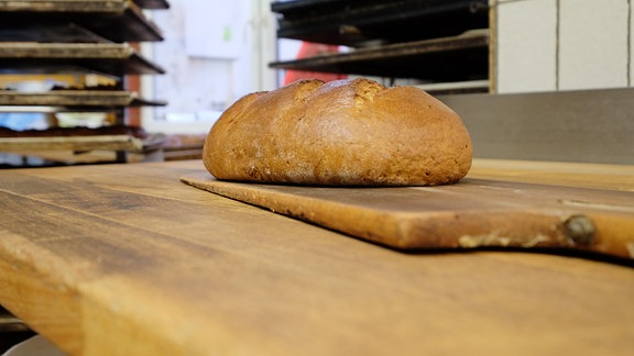 Auf einem Holzschieber liegt ein knusprig braunes Brot.