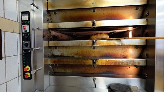 Blick in einen geöffneten Backofen. In einem der Schübe liegt auf einem Holzschieber ein knusprig braunes Brot.