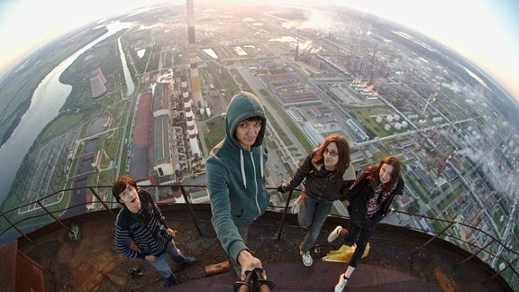 Vier junge Menschen auf einer rostigen Plattform über einem Industriegebiet
