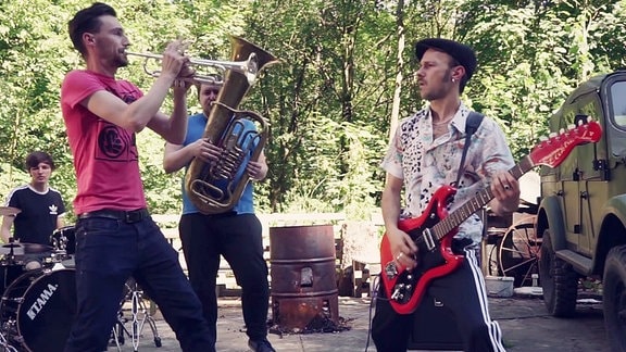 Gruppa Karl-Marx-Stadt: vier Musiker spielen Gitarre, Trompete, Tuba und Schlagzeug unter freiem Himmel