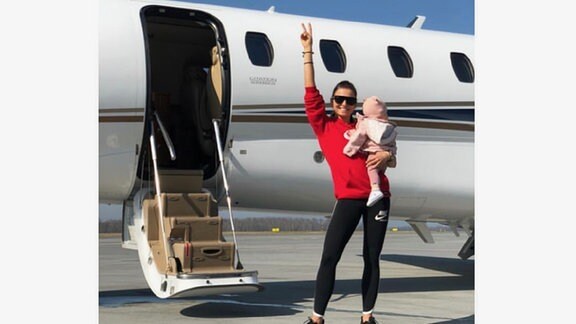 Anna Lewandowska mit ihrer Tochter auf dem Arm vor einem Flugzeug und winkt