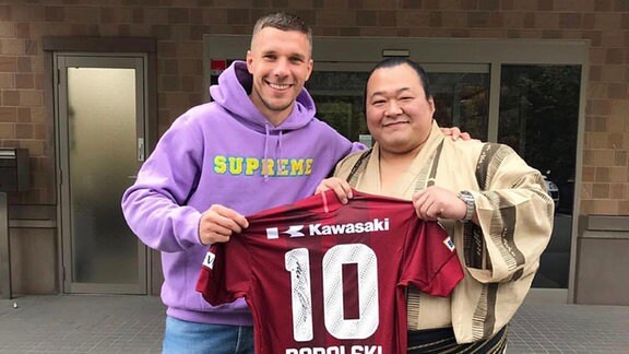 Lukas Podolski steht neben Sumoringer in traditioneller Tracht