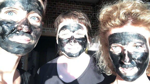 Drei Frauen mit Kohlemaske im Gesicht.