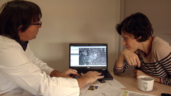Ein Mann in weißen Kittel und eine Frau blicken auf den Monitor eines Laptops