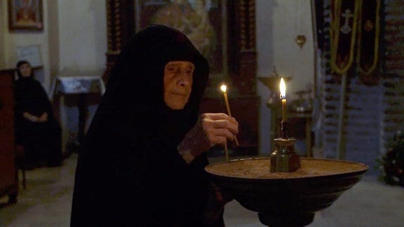 Alte Frau mit Kerze in einer Kirche