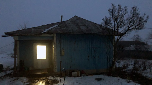 Aus einer Hütte fällt ein Lichtschein auf den Fußweg davor.